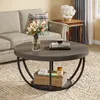 A living room scene featuring a round coffee table with items on it and a basket underneath, placed on a rug in front of a sofa. Produktbild-Vorschau