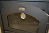 A close-up view of a black wood-burning stove door with a glass window and a thermometer attached. Voir les images du produit