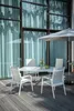 An outdoor dining set with chairs and a table on a wooden deck, with large windows and sheer curtains in the background. Produktbild-Vorschau