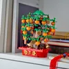 A LEGO model of a lucky chestnut tree decorated with oranges and coins, placed on a shelf next to books. Produktbild-Vorschau