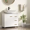 A white bathroom vanity with a vessel sink and a black faucet, a towel on a rack, and a potted plant. Produktbild-Vorschau