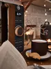 A close-up view of a modern digital microwave with a wooden accent, placed on a table next to a cup of coffee and a book, with fairy lights in the background. Náhled obrázku produktu