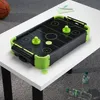 A mini air hockey table is placed on a white table, with a basketball and pens in the background, and water bottles on the floor. Náhľad obrázku produktu