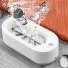A white ultrasonic cleaner is shown with a watch and glasses being cleaned in water. Voir les images du produit