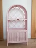 A pink wicker shelf unit with two doors at the bottom, placed against a white wall. Náhľad obrázku produktu
