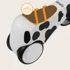A close-up view of the front of a white balance bike with black cow spots and a brown seat with orange straps. Anteprima dell’immagine prodotto