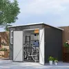 A dark gray garden shed is shown with its doors open, revealing a bicycle, ladder, and shelves with storage boxes inside. The shed is situated outdoors on a paved patio, with a wooden fence and trees in the background. Potted plants are visible to the left Náhľad obrázku produktu