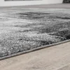 A close-up, low-angle shot of a rug with an abstract pattern, placed on a wooden floor. Produktbild-Vorschau