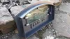 A pizza oven door is placed on rocks and gravel. Produktbild-Vorschau
