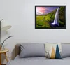 A framed picture of a waterfall hangs on a wall above a bed with pillows and a bedside lamp. Produktbild-Vorschau