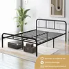 A black metal bed frame is shown in a room with a large plant and two storage boxes underneath. Voir les images du produit
