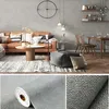 Strukturierte graue Tapete in Rolle und Nahaufnahme, mit Lifestyle-Bild der Anwendung an einer Wohnzimmerwand Náhľad obrázku produktu