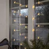 Star-shaped LED lights hanging in a window, with a hint of greenery in the foreground. Podgląd zdjęcia produktu