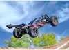 A remote-controlled car is captured mid-air, performing a jump over a dirt ramp, with a blue sky and green trees in the background. Náhľad obrázku produktu