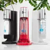 Three soda makers are displayed on a white surface with greenery in the background. Produktbild-Vorschau