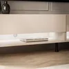 A close-up view of a modern white TV cabinet with black legs, featuring a book on a shelf and subtle LED lighting. Náhled obrázku produktu