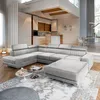 A modern, spacious living room with a large sectional sofa and ottoman, featuring a minimalist aesthetic. In the background, a contemporary kitchen and dining area are visible, with large windows providing natural light. Podgląd zdjęcia produktu