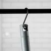 A close-up of a gray cleaning tool handle hanging from a black hook on a black rod, with a blurred white brick wall in the background. Podgląd zdjęcia produktu