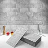 Gray stone-look peel and stick wall tiles stacked on a white kitchen counter with a faucet and fruit Produktbild-Vorschau