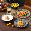 A table setting with a colorful tableware set, including plates, bowls, and a glass of drink. Náhled obrázku produktu