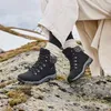 A person wearing black boots and beige pants is sitting on a rocky surface with snow in the background. Anteprima dell’immagine prodotto