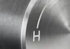 A close-up of a brushed metal dial with an 'H' marking. Produktbild-Vorschau