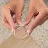 Hands applying a clear corner protector to the edge of a wooden table. Produktbild-Vorschau
