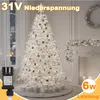 A decorated white Christmas tree with lights, gifts underneath, and a fireplace with garland and wreath in the background. A power adapter is shown in the foreground. Anteprima dell’immagine prodotto
