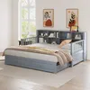 A gray daybed with a bookshelf headboard is shown in a bedroom setting with artwork on the wall and a window in the background. Náhled obrázku produktu