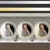 Three identical round mirrors with LED lighting are displayed above bathroom sinks, each reflecting a woman in a bathrobe. Voir les images du produit