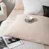 A close-up view of a bed with beige musselin bedding, white and black pillows, and a magazine. Podgląd zdjęcia produktu