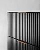 A close-up view of a black cabinet with ribbed doors and gold handles, against a light gray background. Voir les images du produit
