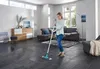 A woman is mopping a dark tiled floor in a modern living room. Produktbild-Vorschau