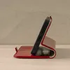 A red leather phone case with a phone inserted, propped up in a stand position. Produktbild-Vorschau