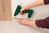 A person is using a green cordless hot glue gun to apply glue to a piece of trim. Produktbild-Vorschau
