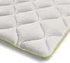 A close-up, angled view of a white mattress topper with a quilted pattern and a yellow trim. Náhled obrázku produktu