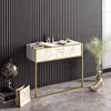 A modern console table with a marble-effect drawer front and gold frame, set against a slatted black wall. Decorative items like a globe, books, a paper bag, and high heels are placed around it, suggesting a stylish entryway or dressing area. Produktbild-Vorschau