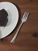 A slice of chocolate cake on a white plate next to a silver fork on a wooden table. Anteprima dell’immagine prodotto