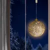 A glowing Christmas ornament hangs in a window overlooking a snowy forest at night. Náhled obrázku produktu