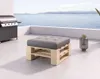 A pallet ottoman with a grey cushion sits on a patio overlooking the ocean, with a grill to the left and a lantern to the right. Produktbild-Vorschau