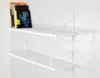A white two-tiered shelf with decorative metal scrollwork is mounted on a white wall. Three books are placed on the top shelf. Náhľad obrázku produktu