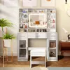 A white vanity table with a lighted mirror and shelves filled with makeup and skincare products, a white stool in front, and plants in the background. Voir les images du produit