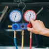 A hand is shown adjusting a car air conditioning manifold gauge set, which is hanging from a hook. Produktbild-Vorschau