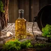 A bottle of liquid sits on a rustic wooden surface with straw, moss, and a dark pot. Voir les images du produit