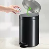 A hand is shown dropping a crumpled piece of paper into a black pedal bin. A green arrow indicates the lid opening. Podgląd zdjęcia produktu