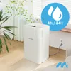 A white dehumidifier is shown in a room with a window and curtains. Leaves are depicted blowing in the wind, and a blue circle with water droplets and text is overlaid on the image. Voir les images du produit