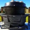 A black cast iron grill pot with a lid filled with charcoal sits on a black grill base outdoors. Podgląd zdjęcia produktu