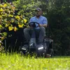 A man is riding a lawnmower in a grassy area with trees in the background. Produktbild-Vorschau