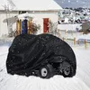 A black lawnmower cover is shown on a snowy lawn in front of a house with a white exterior and blue and red doors. It is snowing. Produktbild-Vorschau