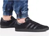 A person wearing black Adidas Gazelle sneakers and blue jeans. Voir les images du produit